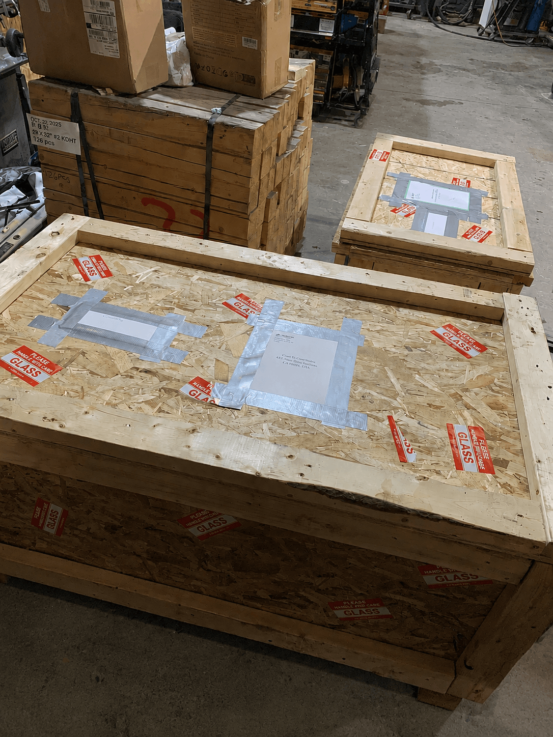 Custom-built wooden shipping crates covered in "Handle With Care — Glass" labels in the facility.