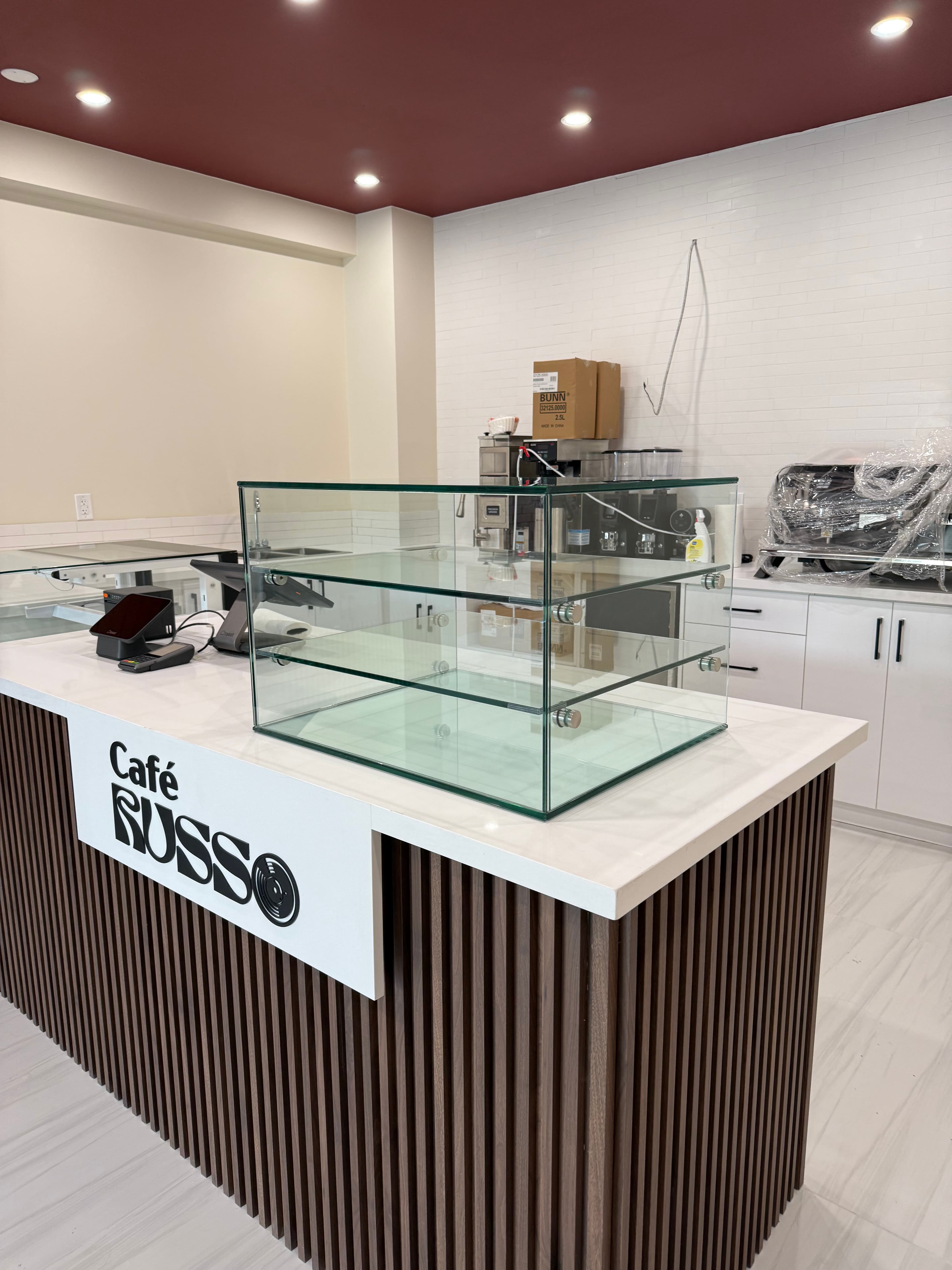 Frameless glass display case on a wood-slat base at Café Russo, with the POS counter visible behind it.