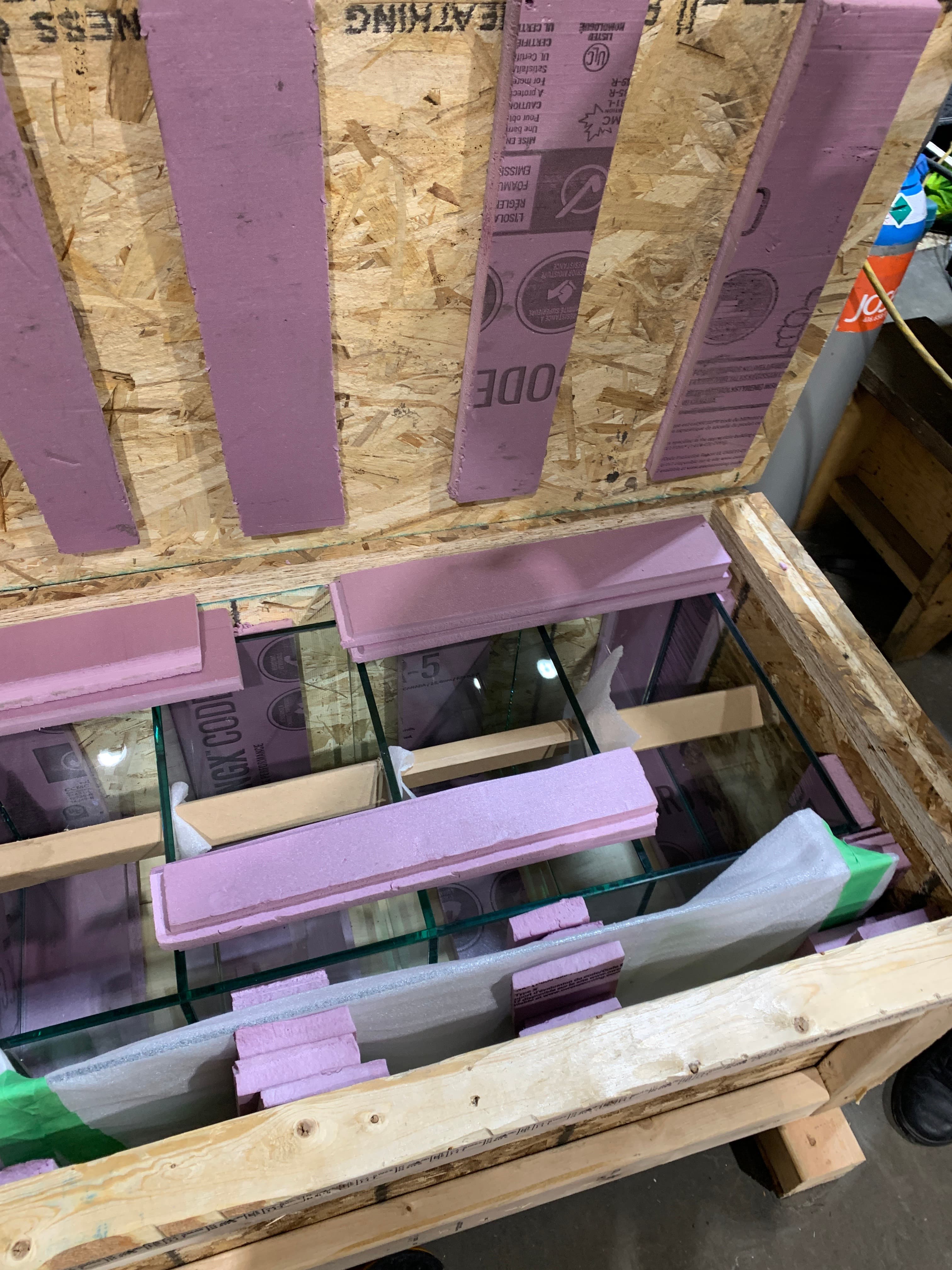 Top-down view into an open crate showing glass panels separated and braced with foam spacers.