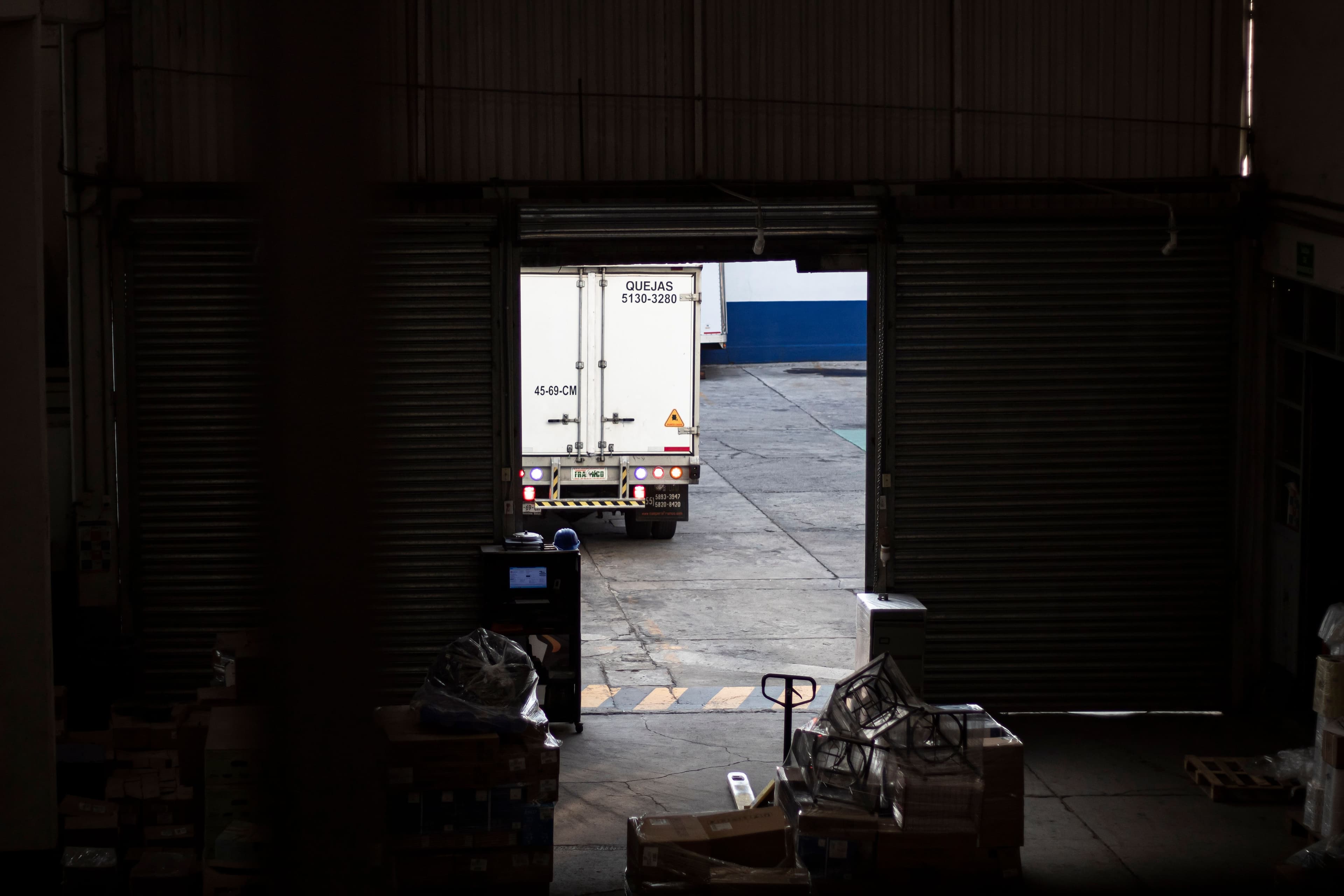 A freight box truck viewed from inside the warehouse through an open loading-dock door.