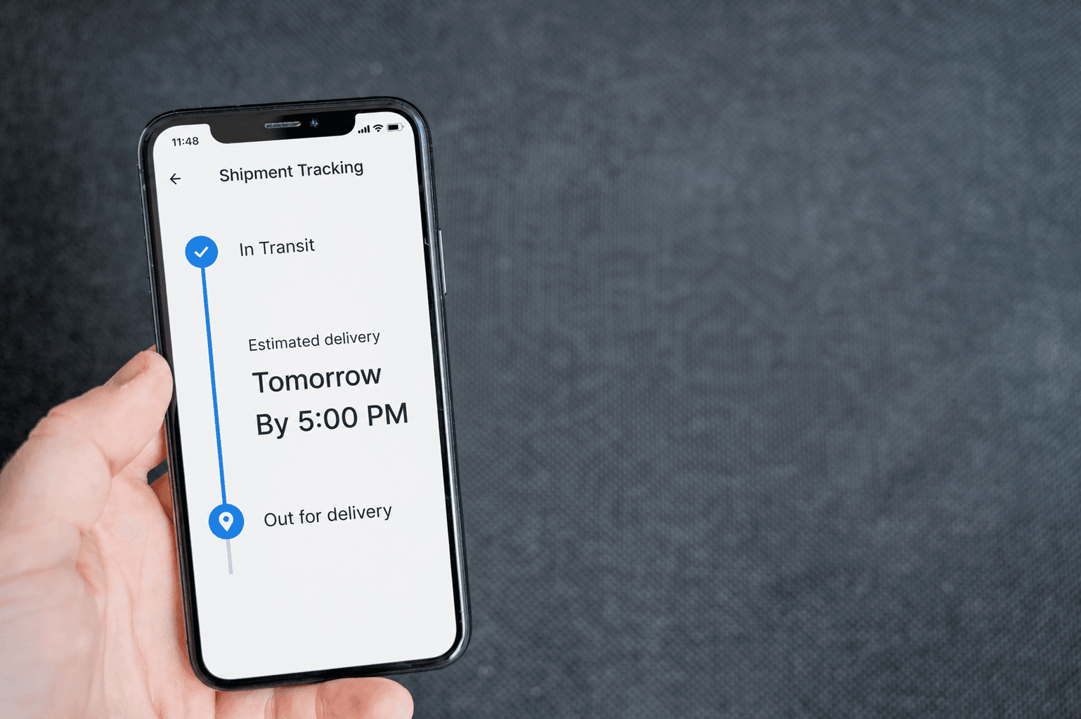 A hand holding a phone showing a shipment tracking screen with an estimated delivery time.
