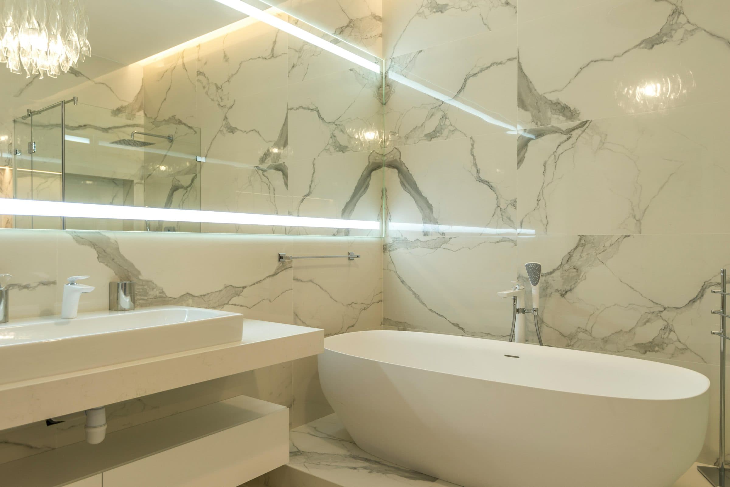 Illuminated LED mirror and backlit frosted glass strips above a marble vanity beside a freestanding bathtub, fabricated and installed by 6 Sigma Interiors