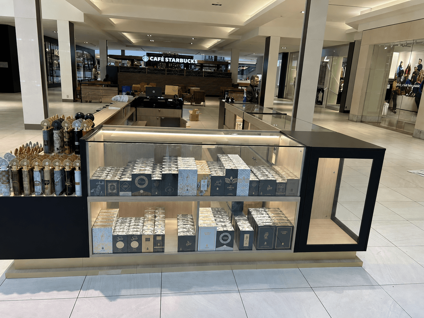 Illuminated custom glass and wood retail display kiosk showcasing rows of perfume boxes in a shopping mall
