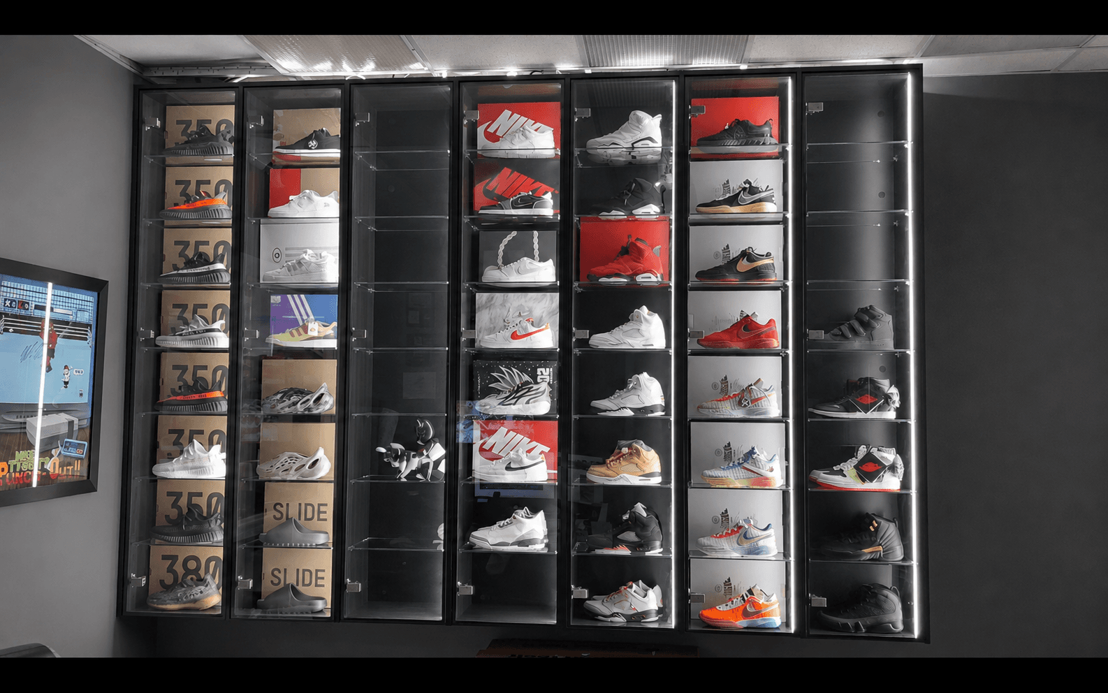 Illuminated glass display cases lining a retail showroom wall, each shelf lit to showcase sneakers and collectibles